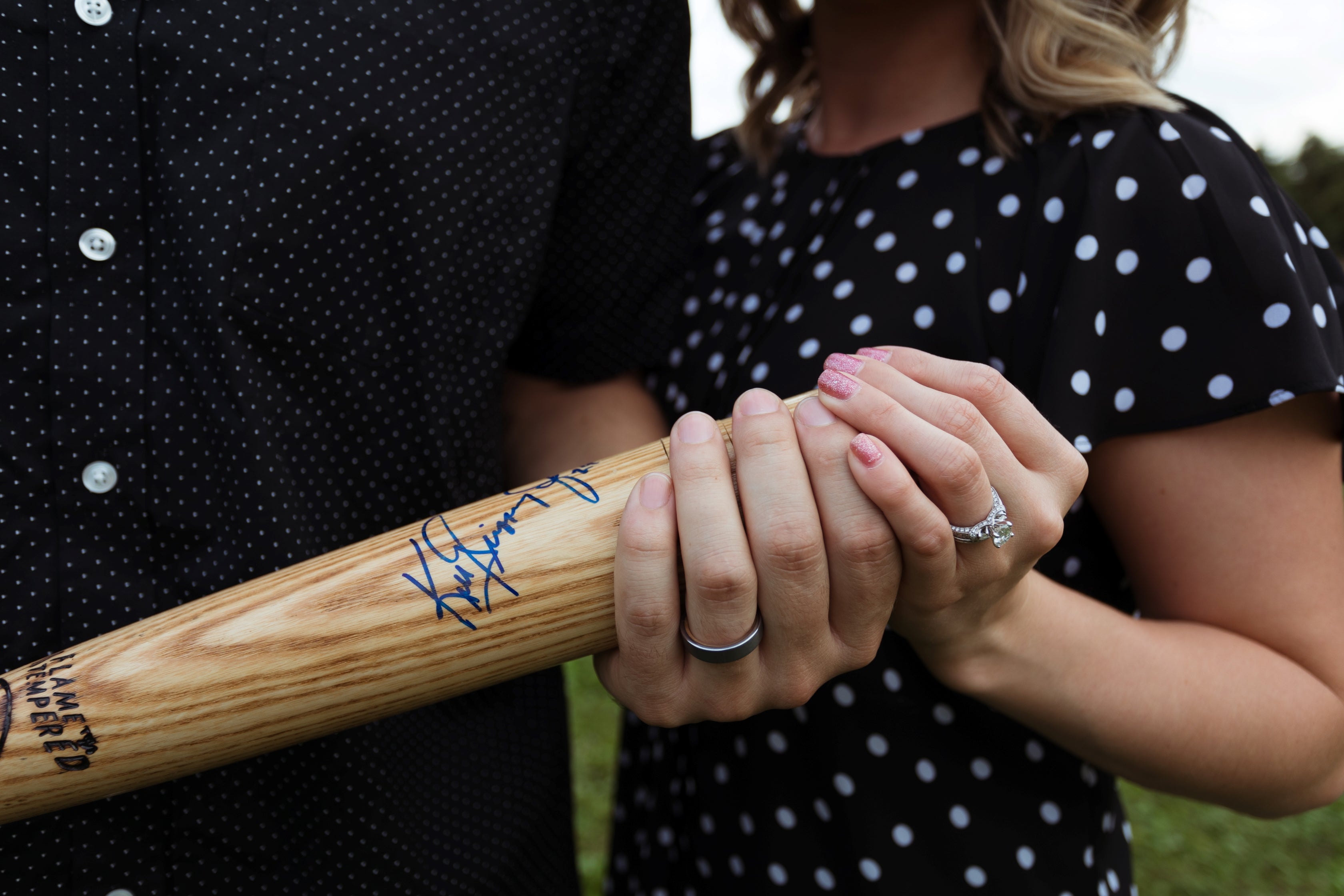 Couple holding a baseball bat used in ring on his finger
