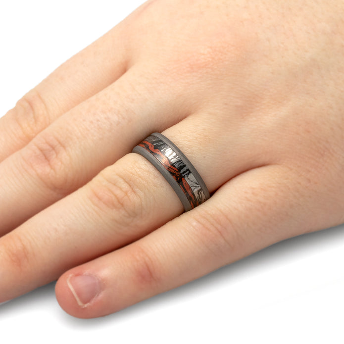 Hand wearing a silver ring with a red and black design on a white background