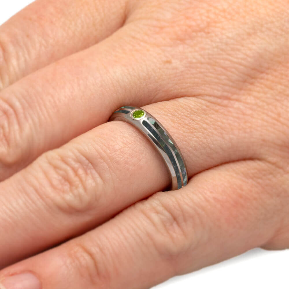 Titanium men's wedding band with crushed peridot and pearl inlays, worn on hand, highlighting the bezel-set green birthstone.