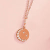 Rose gold diamond crescent moon necklace on pink background
