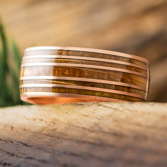 Rose gold whiskey barrel wedding band on wood surface