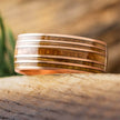 Rose gold whiskey barrel wedding band on wood surface