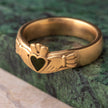 Gold ring with a hand and heart design on a green stone surface