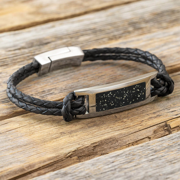 Black braided leather bracelet with metallic clasp on a wooden surface