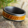 Gold and black zirconium wedding band with whiskey oak inlay, 8mm wide, featuring a beveled profile and matte finish, displayed on a stone surface.
