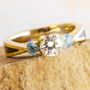 Topaz and Moissanite Engagement Ring with Goldstone Inlay featuring a round-cut center stone and two Swiss blue topaz side stones in yellow gold.