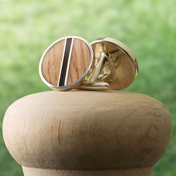 Baseball Bat Cuff Links with black enamel stripe and game-used wood on a silver base, displayed on a wooden stand outdoors.