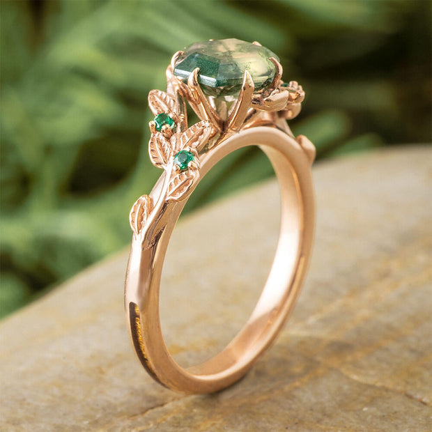 Rose gold ring with green gemstones on a stone surface with a blurred green background