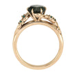 Rose gold ring with a central green gemstone and smaller emeralds on a white background