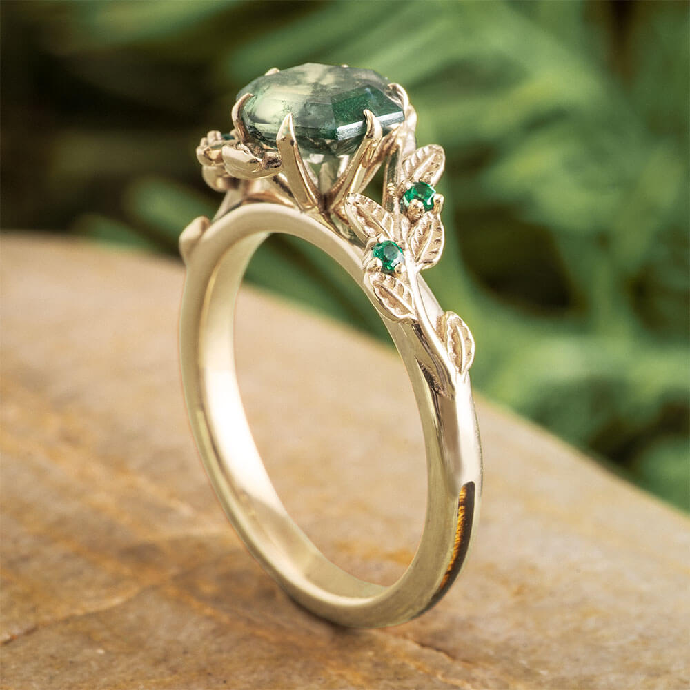Gold ring with green gemstone on a wooden surface with a blurred green leafy background