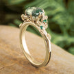 Gold ring with green gemstone on a wooden surface with a blurred green leafy background