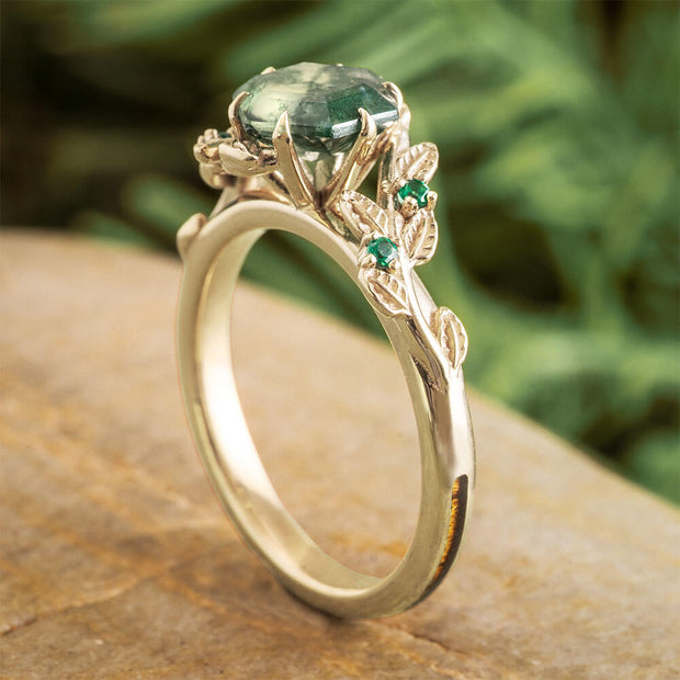 Gold ring with green gemstone on a wooden surface with a blurred green leafy background