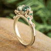 Gold ring with green gemstone on a wooden surface with a blurred green leafy background