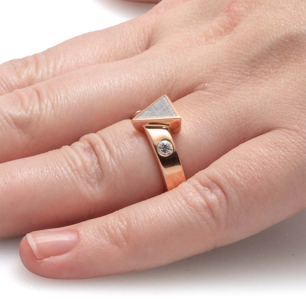 Rose gold ring with a diamond on a finger against a white background