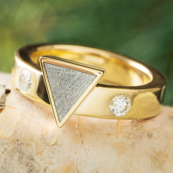 Gold ring with a triangular stone and embedded diamonds on a natural stone surface.