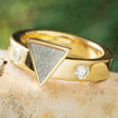 Gold ring with a triangular stone and embedded diamonds on a natural stone surface.