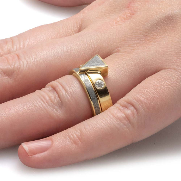 Gold ring with geometric design on a finger against a white background