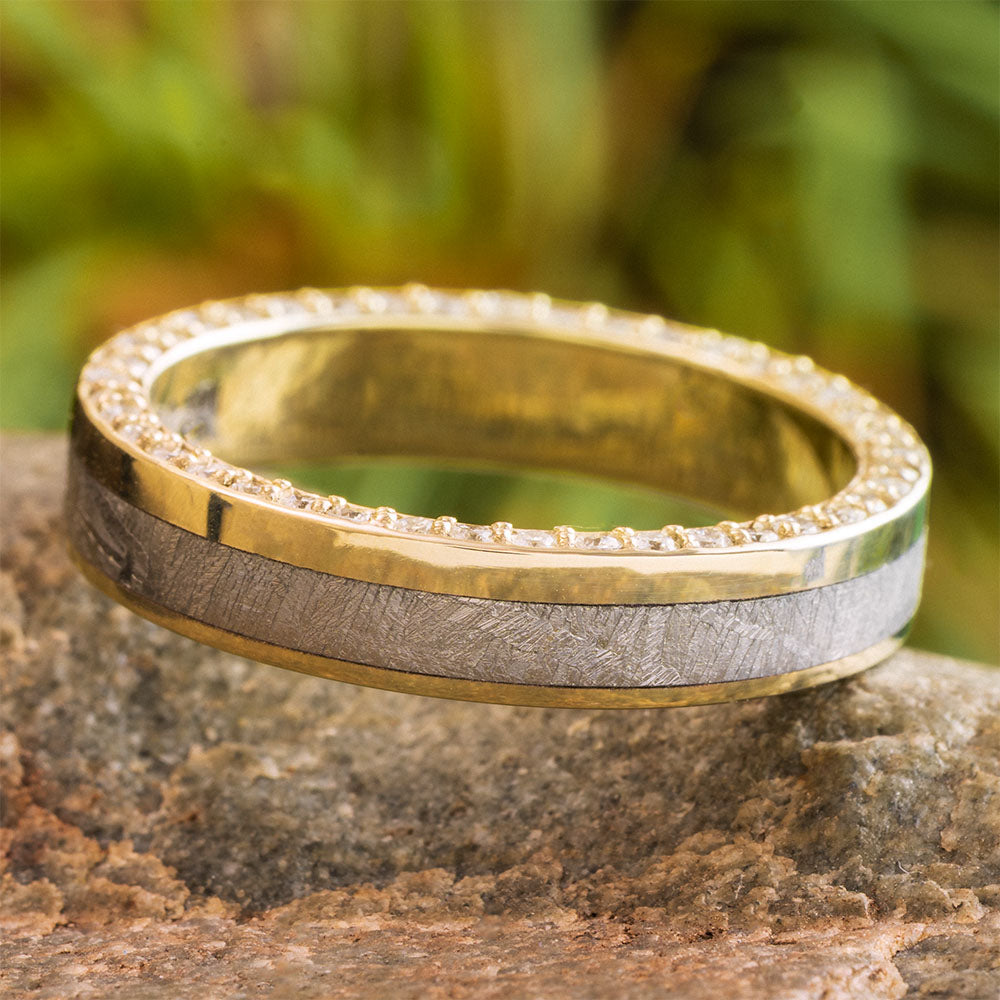 Two-tone gold and silver ring on a stone surface with a blurred green background