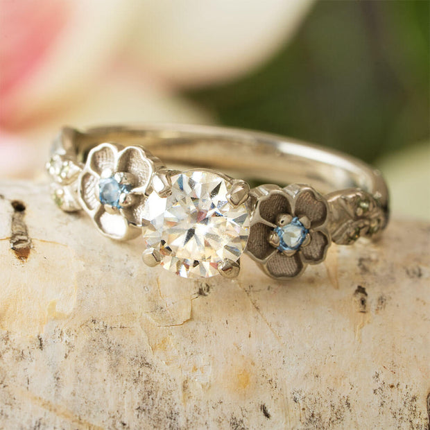 Silver ring with floral designs and gemstones on a stone surface