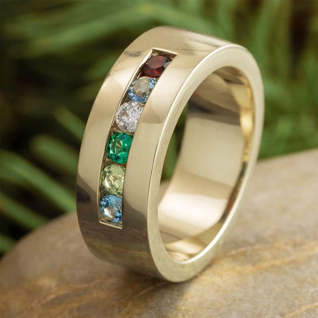 Gold ring with colorful gemstones on a stone surface with green foliage in the background