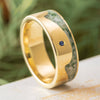 Gold ring with a blue gemstone on a wooden surface with greenery in the background