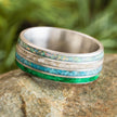 Multicolored ring with green and blue inlay on a stone surface with a blurred natural background