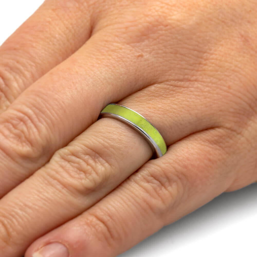 Close-up of a hand wearing a ring with a green band on a plain background