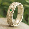 Gold ring with green gemstone on a wooden surface with a blurred green background