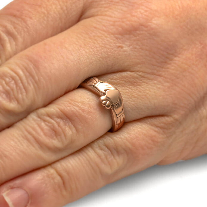 Rose gold ring with a foot design on a hand against a white background