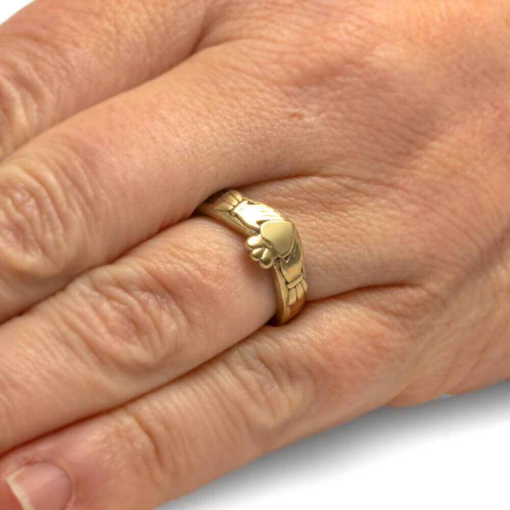 Gold ring with a unique design on a person's finger against a neutral background