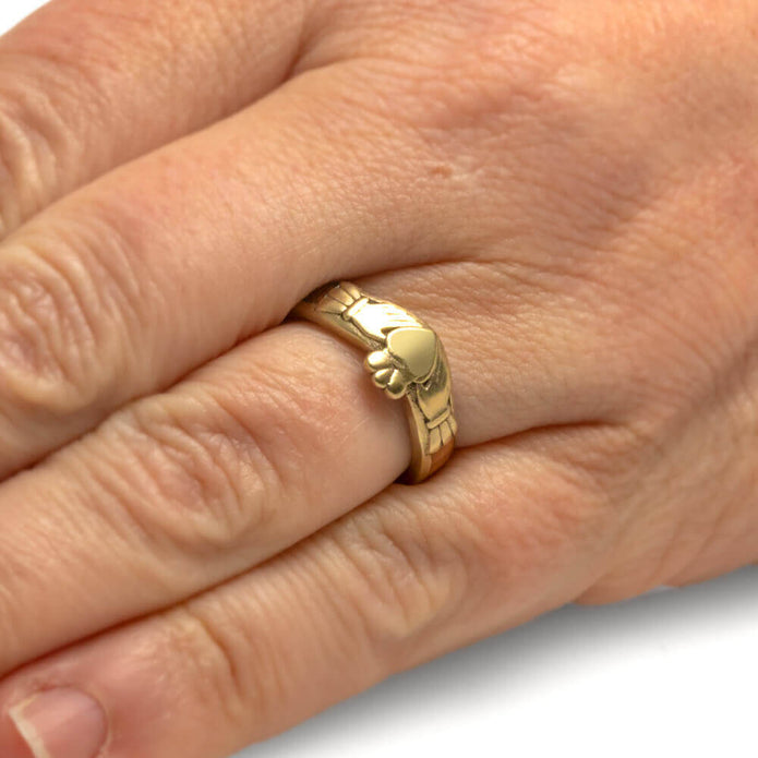Gold ring with a unique design on a person's finger against a neutral background
