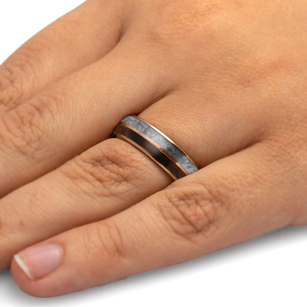 Hand wearing a silver ring with a rose gold band on a white background