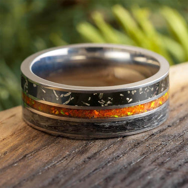 Silver ring with black and orange inlay on a wooden surface with blurred green background