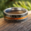 Silver ring with black and orange inlay on a wooden surface with blurred green background