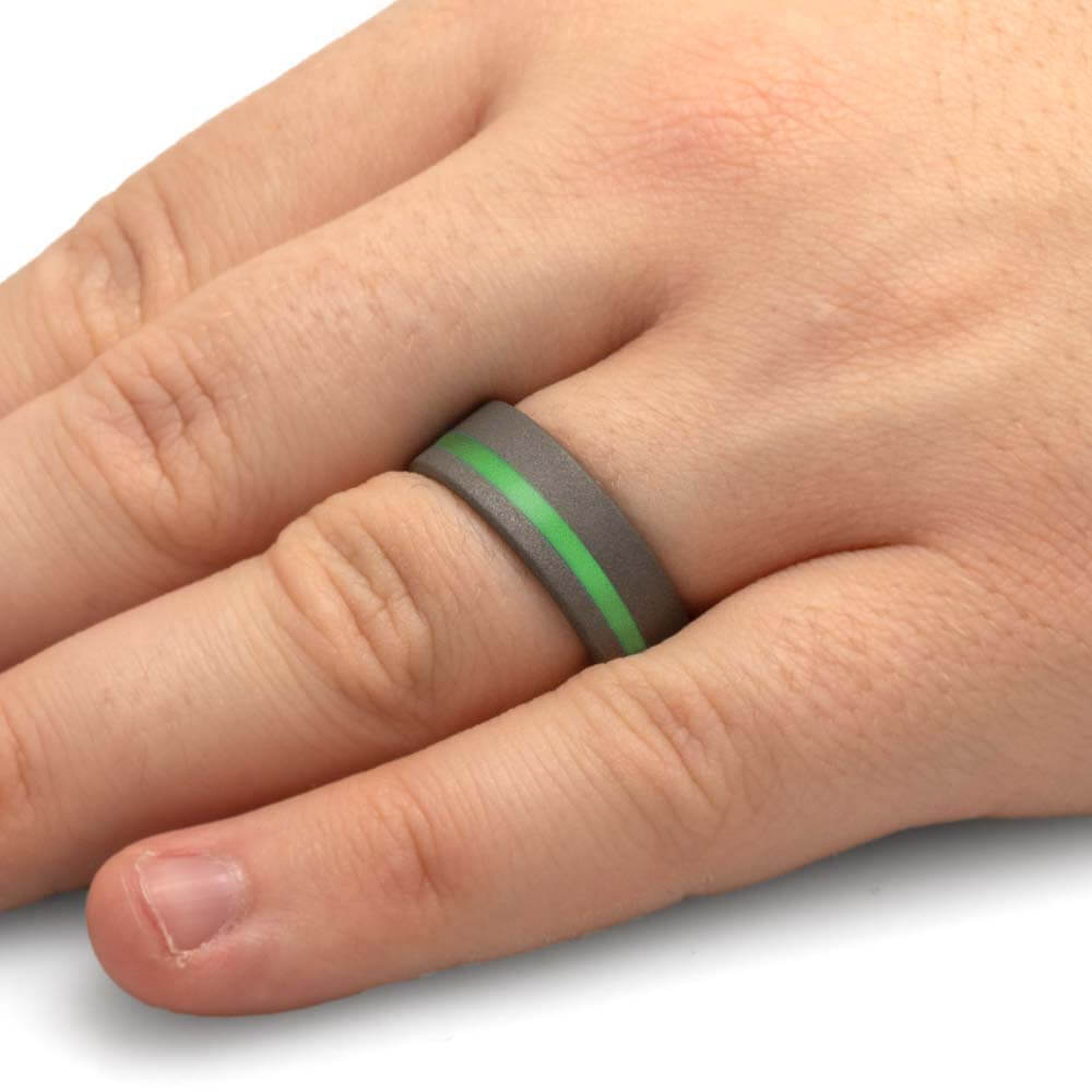 Gray ring with a green stripe on a person's finger against a white background