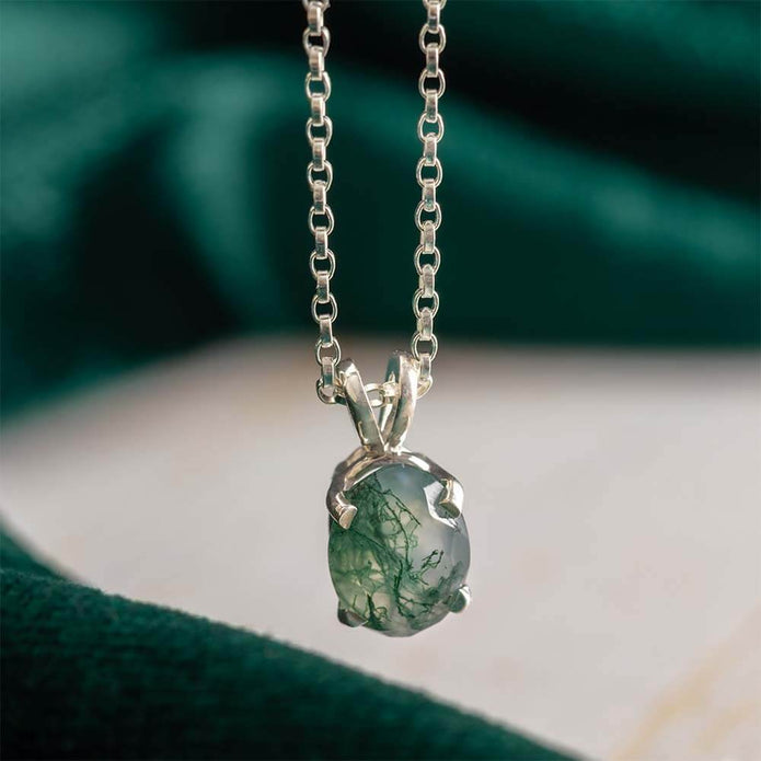 Silver necklace with a green pendant on a blurred green and beige background