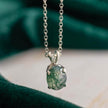 Silver necklace with a green pendant on a blurred green and beige background