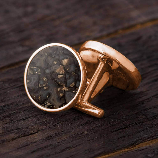 Rose gold cufflinks with a textured black stone on a wooden surface