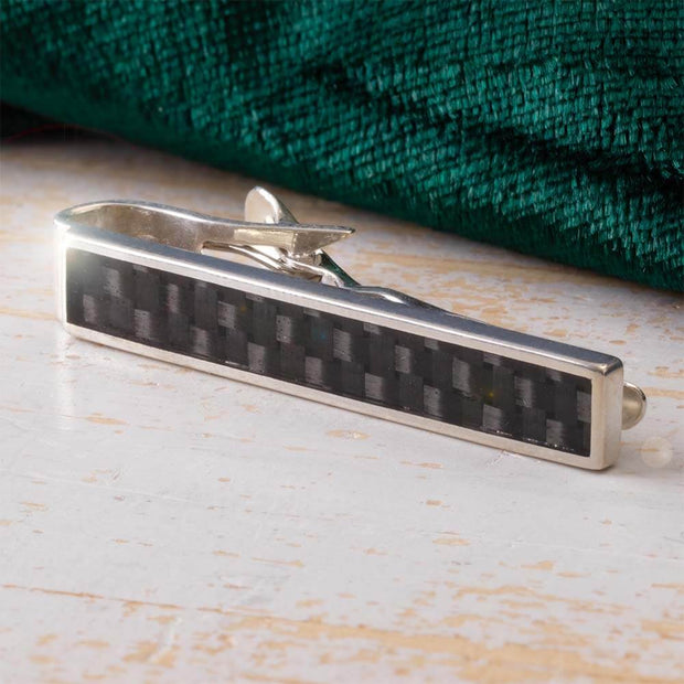 Silver tie clip with carbon fiber pattern on a wooden surface