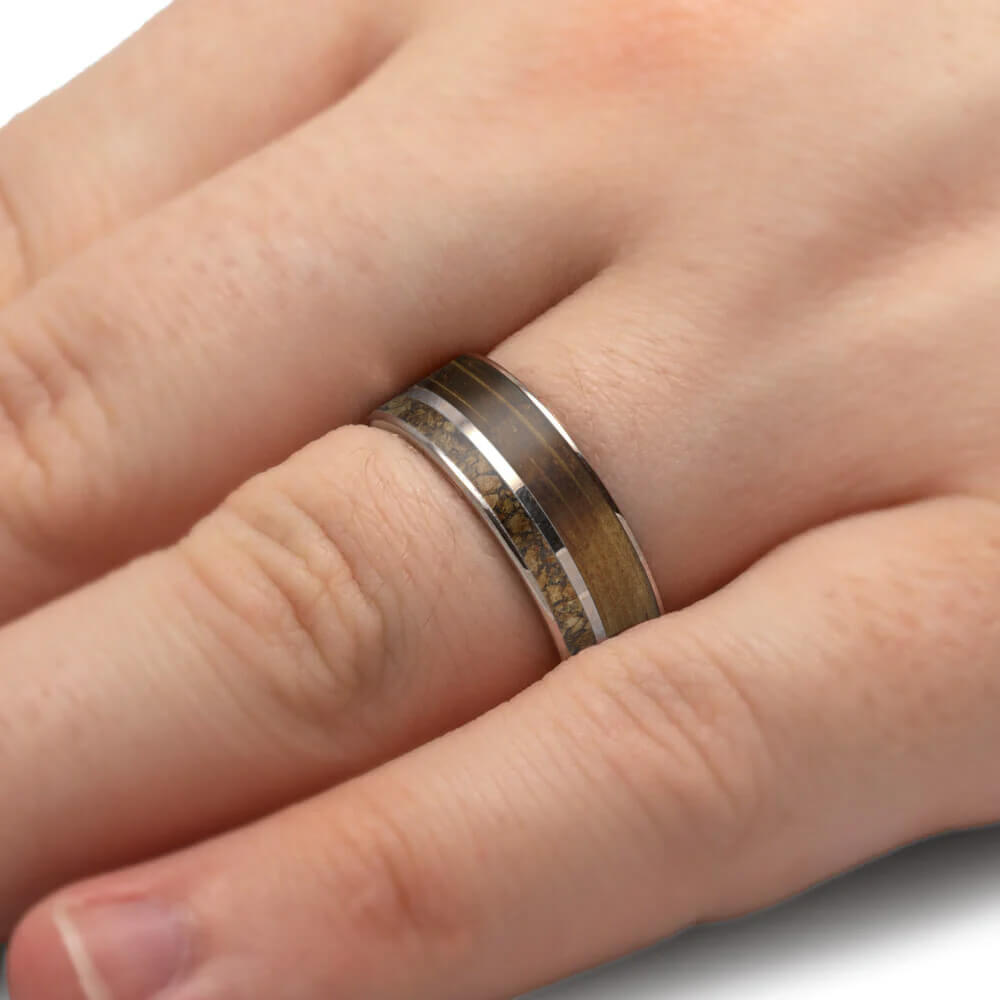 Close-up of a hand wearing a silver ring with a wooden band on a neutral background