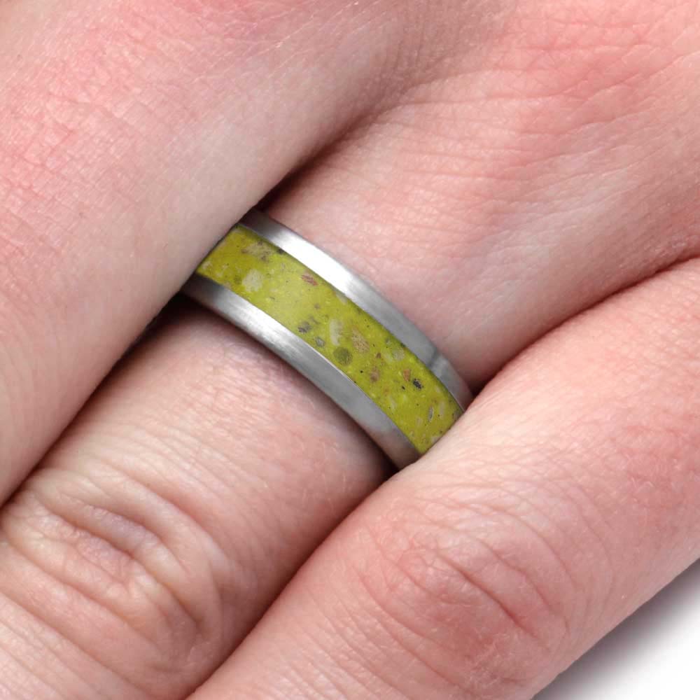 A close-up of a hand wearing a silver band ring with a textured yellow-green inlay.