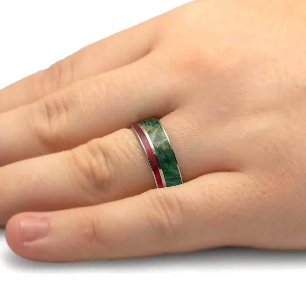 A close-up of a hand wearing a slim silver band ring with a green inlay and a red stripe.