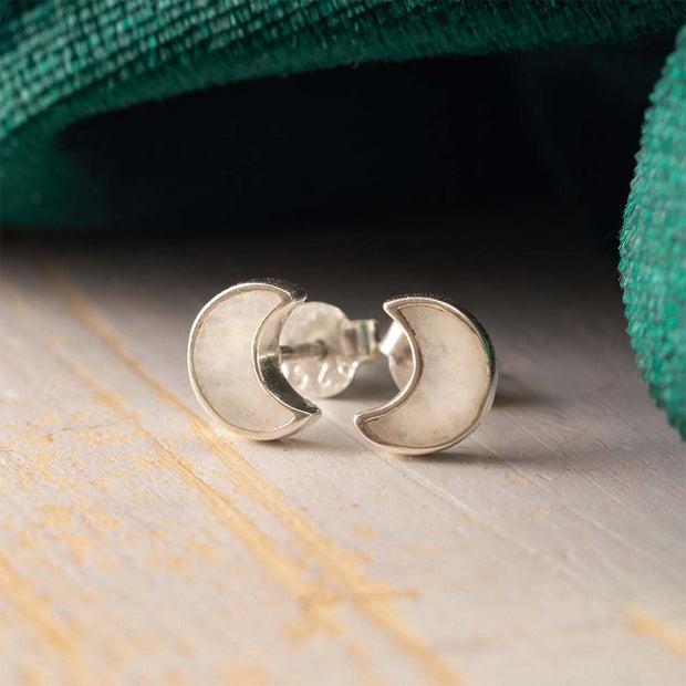 Silver crescent moon earrings on a wooden surface with green fabric in the background