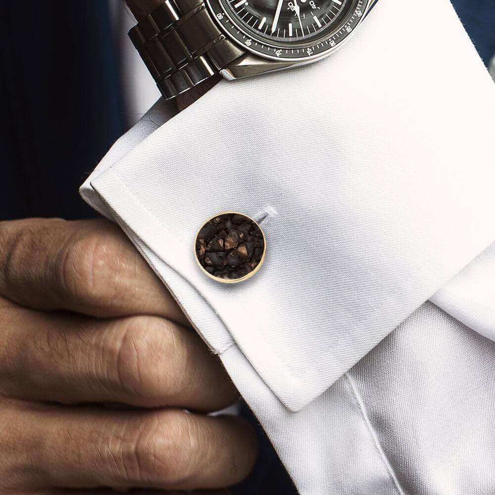 Close-up of a cufflink on a white shirt with a watch on the wrist.