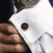 Close-up of a cufflink on a white shirt with a watch on the wrist.