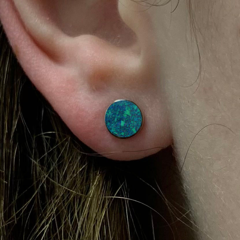 Blue-green opal stud earring worn on ear, showcasing vibrant synthetic opal in sterling silver. Add color to your look with these gemstone earrings.