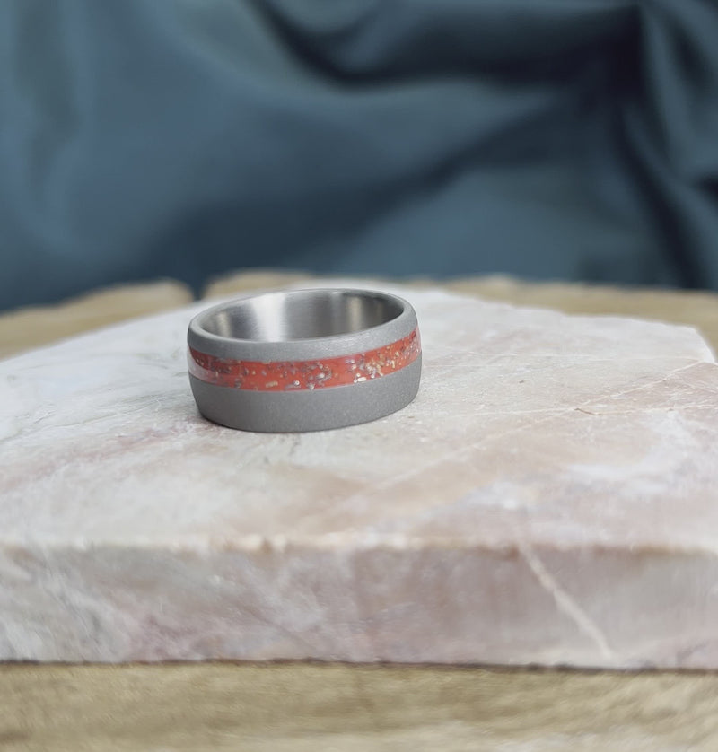 Titanium wedding band with red meteorite stardust on stone.