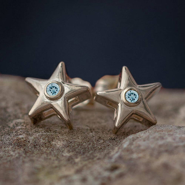 Gold star stud earrings with light blue birthstone