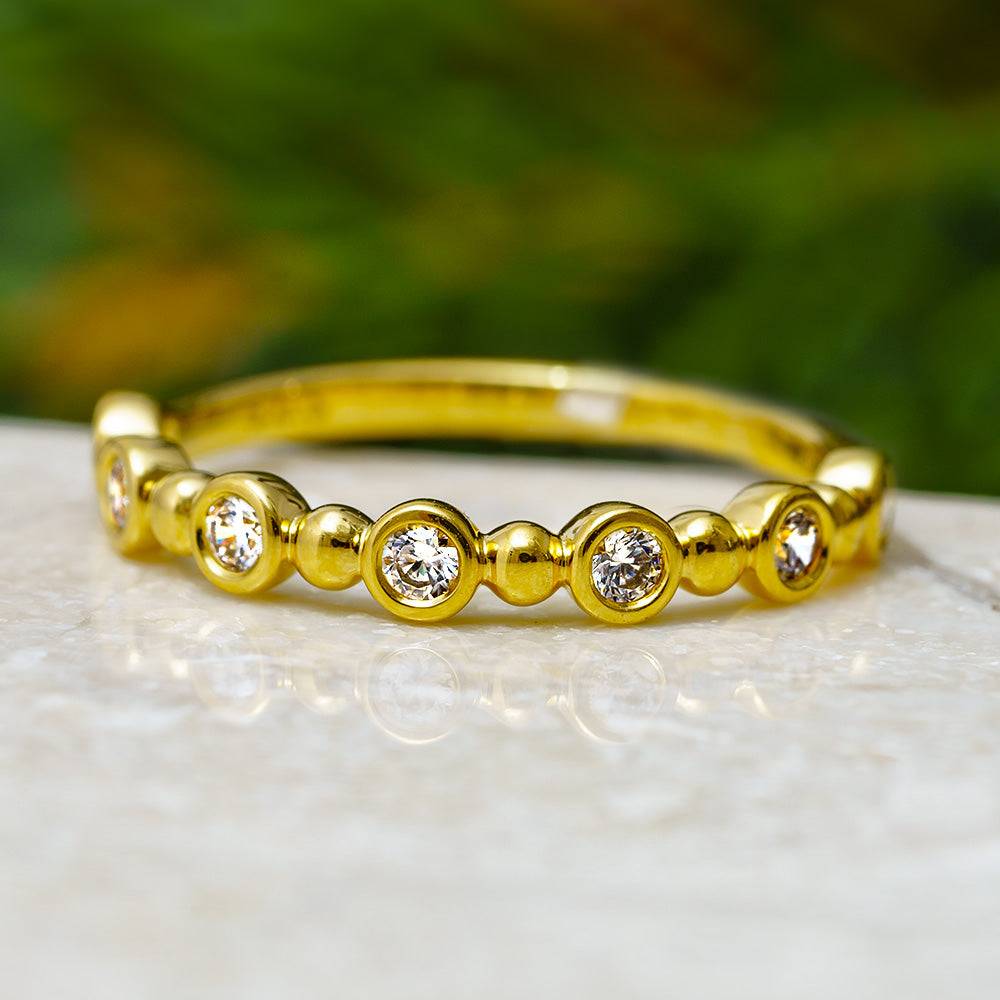 Bezel set diamond band with gold ball accents on marble surface